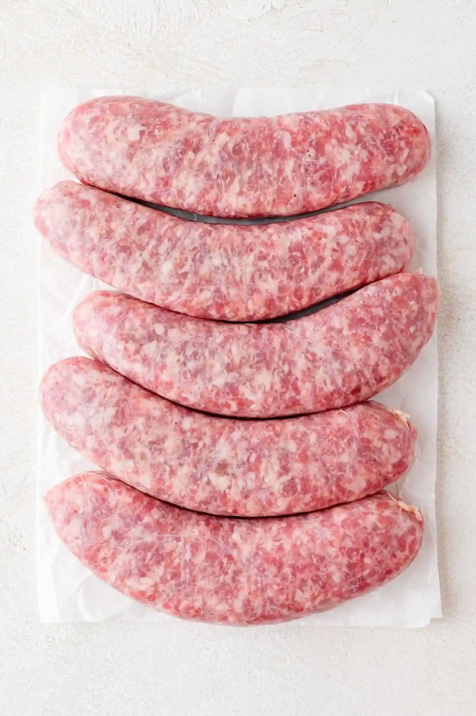 Five uncooked brats on a white surface.