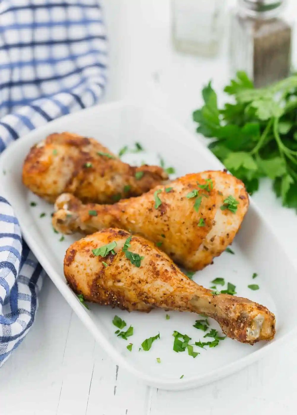 Three cooked drumsticks on a white serving plater, on a white wooden background.