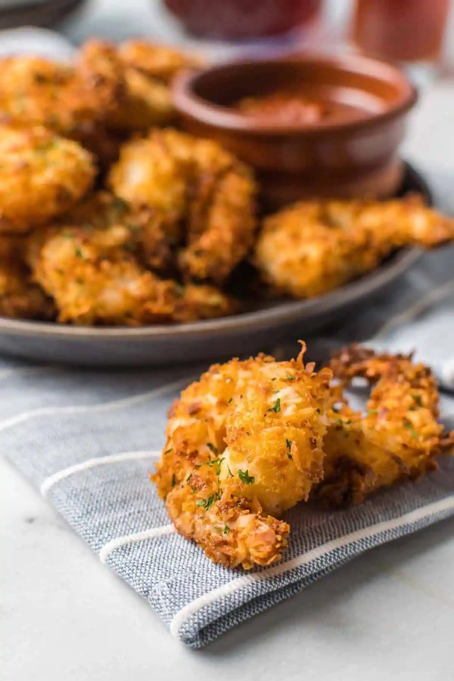 Two crispy shrimp in front of a plate full of more.