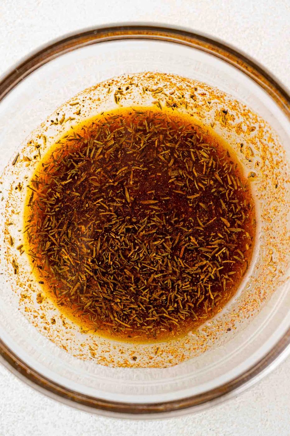 A glass bowl containing a brown liquid mixture with herbs and spices.