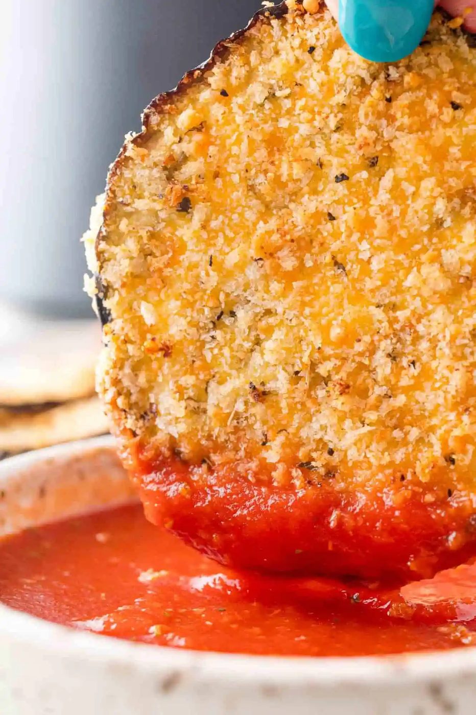 Slice of air fryer eggplant being dipped in marinara sauce.