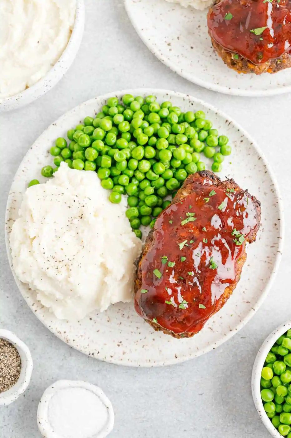 Air fryer meatloaf on a plate with peas and mashed potatoes.