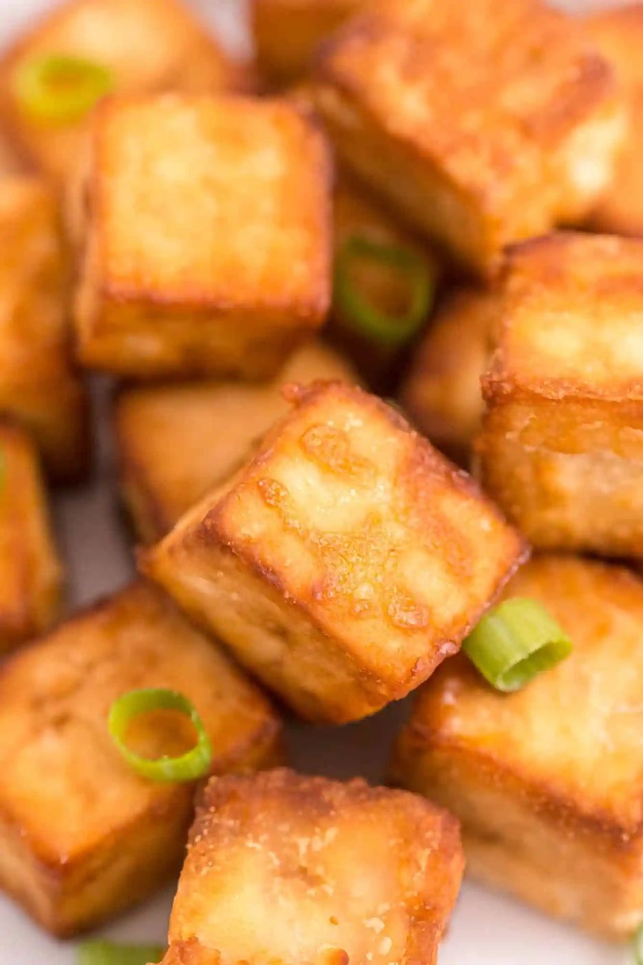 Close up of cubed, crispy tofu on a plate, topped with green onions.