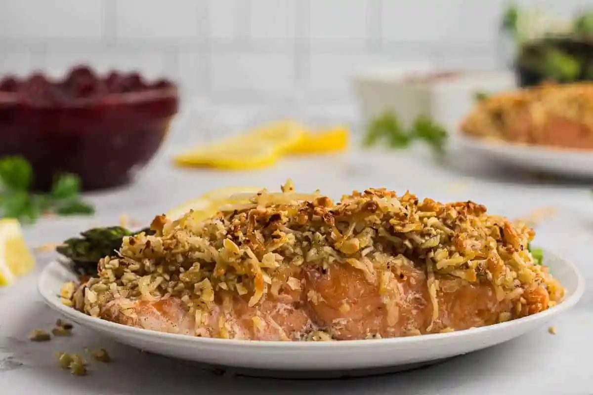 Close up of cooked salmon on a plate. Salmon is crusted with almonds and parmesan cheese.