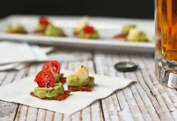 Trio of appetizers on paper napkin with white rectangular tray of appetizers in background.