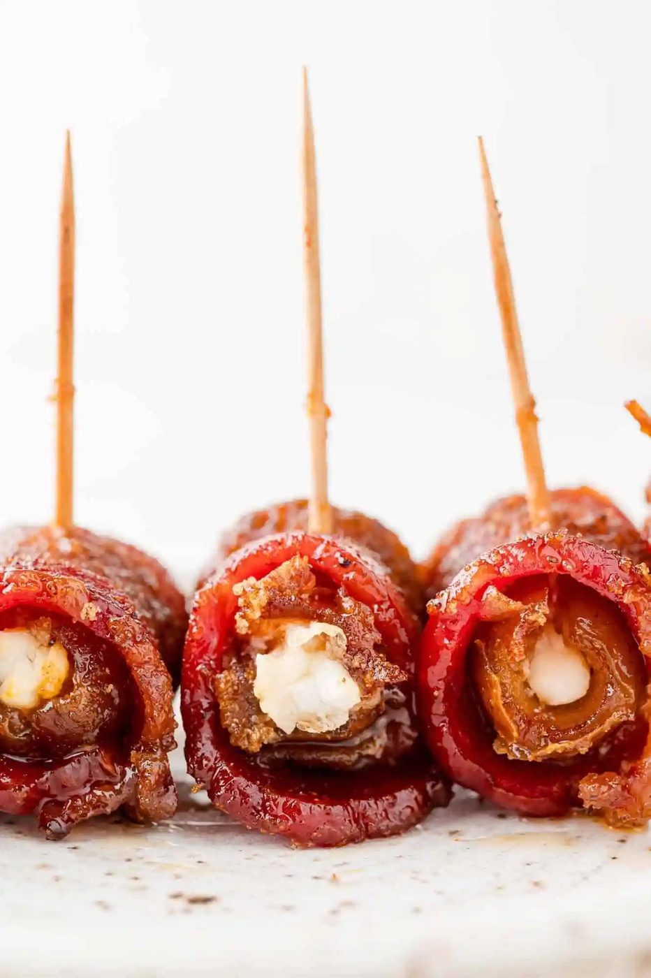 Three bacon wrapped dates on a plate, turned to show filling.