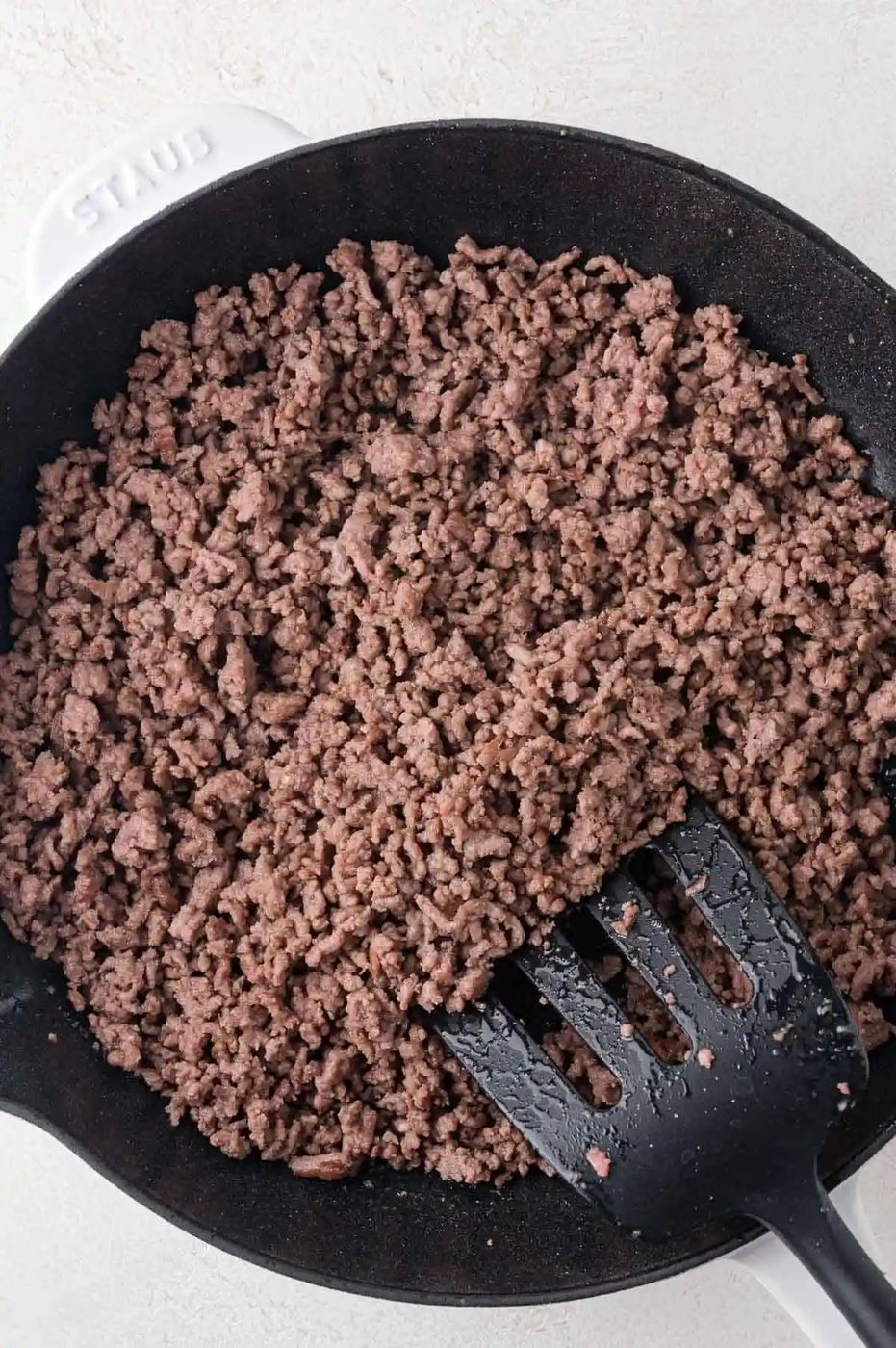 Cooked ground beef in a black skillet, with a black spatula resting inside.
