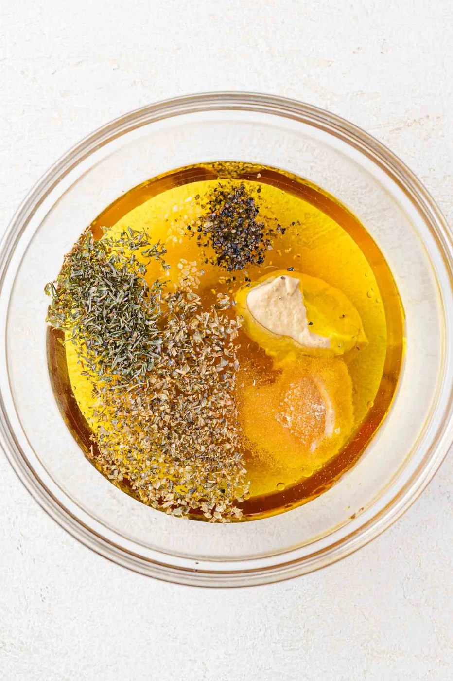 A glass bowl containing salad dressing ingredients on a white surface.