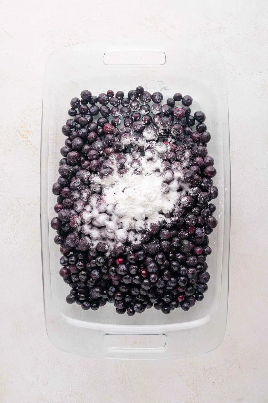 A glass baking dish filled with blueberries topped with a mound of cornstarch and sugar.