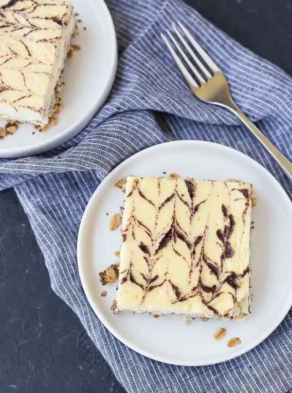 Overhead of a serving of breakfast cheesecake on round white plate with fork and striped blue cloth.