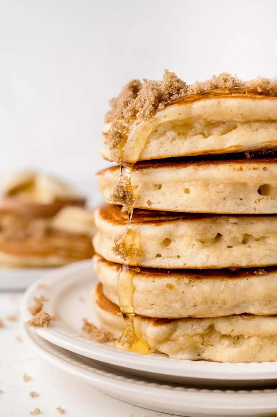 A stack of five golden-brown pancakes topped with crumbled brown sugar and syrup on a white plate.