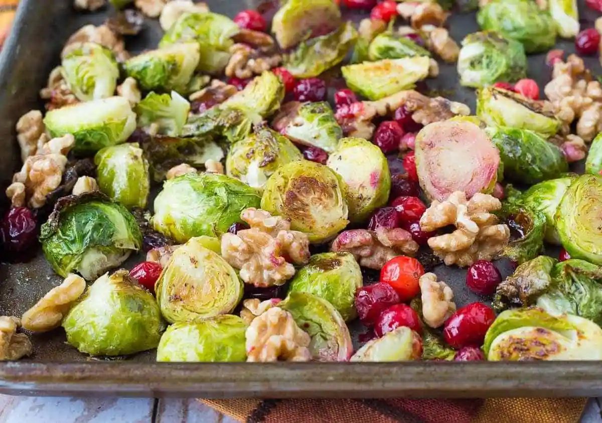 Partial overhead of roasting pan containing roasted brussels sprouts, walnuts, and cranberries.