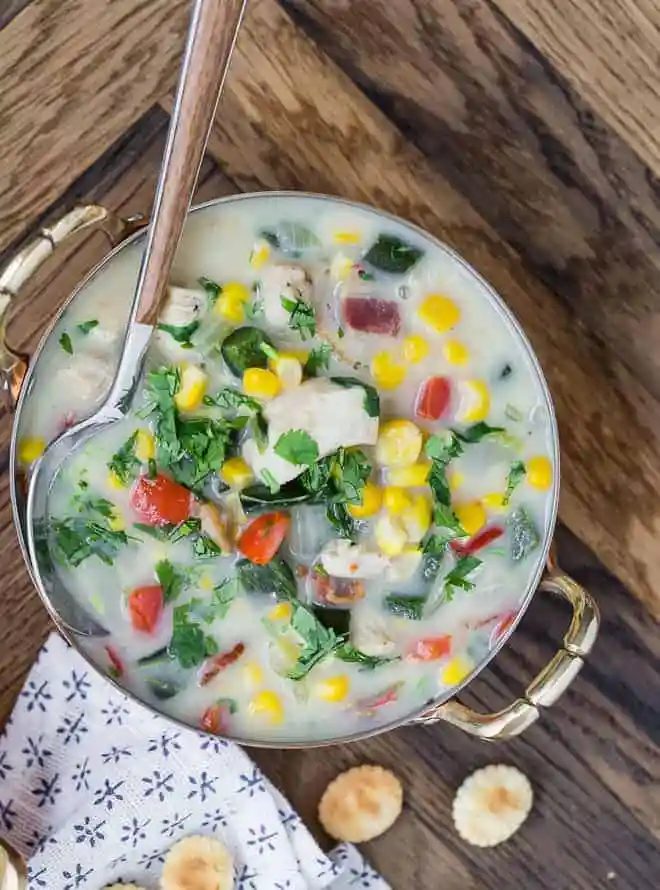 Close up overhead view of chicken corn chowder, in a two-handled bowl, with a spoon.