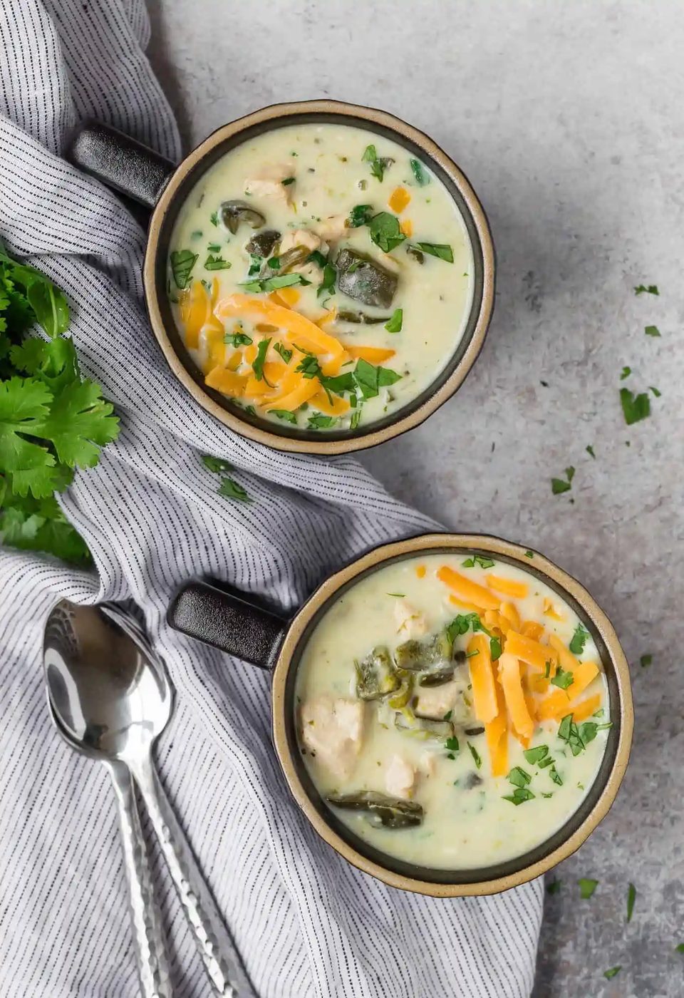 Two black mugs full of chile relleno soup topped with cheddar cheese.