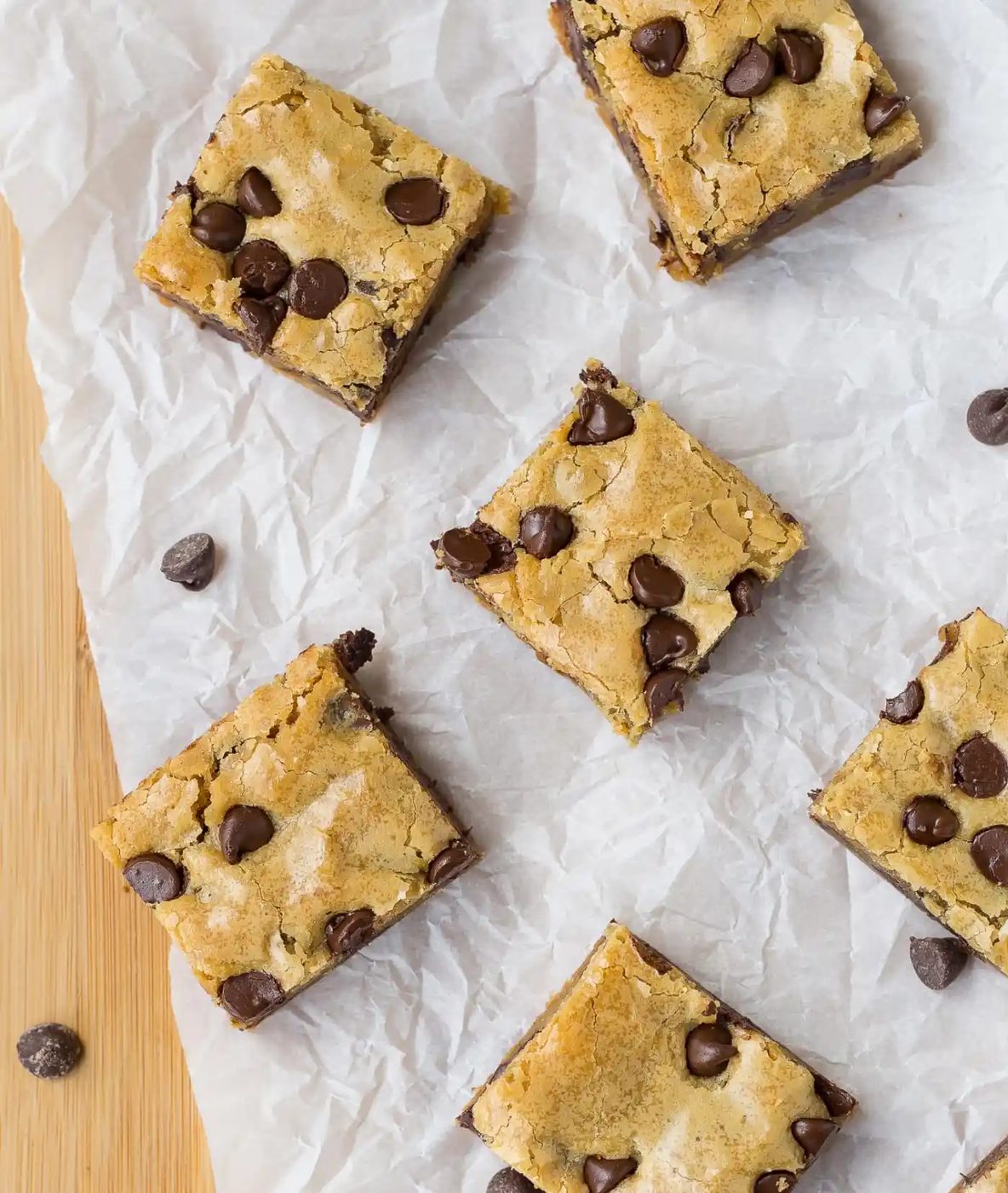 Five chocolate chip cookie bars arranged on crumpled parchment paper, with a few chocolate chips scattered nearby.