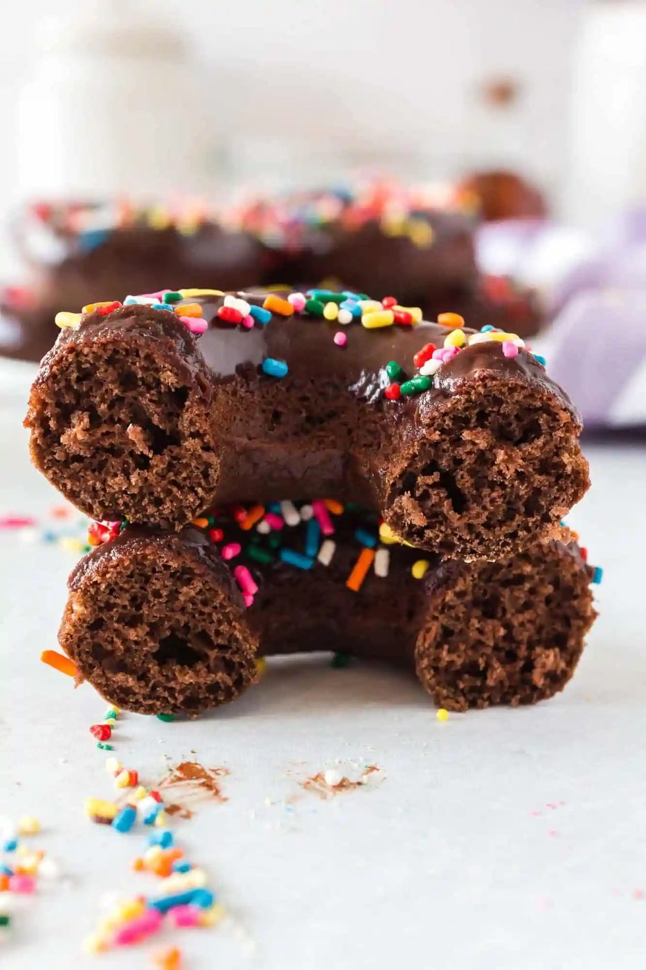 Two stacked chocolate donut halves with colorful sprinkles on a light surface.