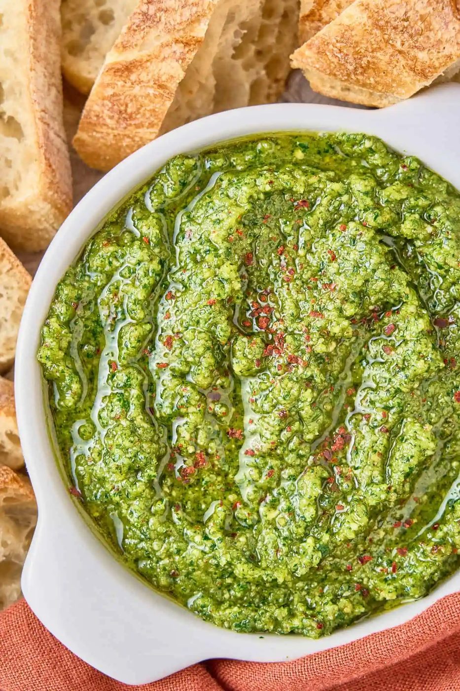 Cilantro pesto in a white bowl, surrounded by slices of bread.