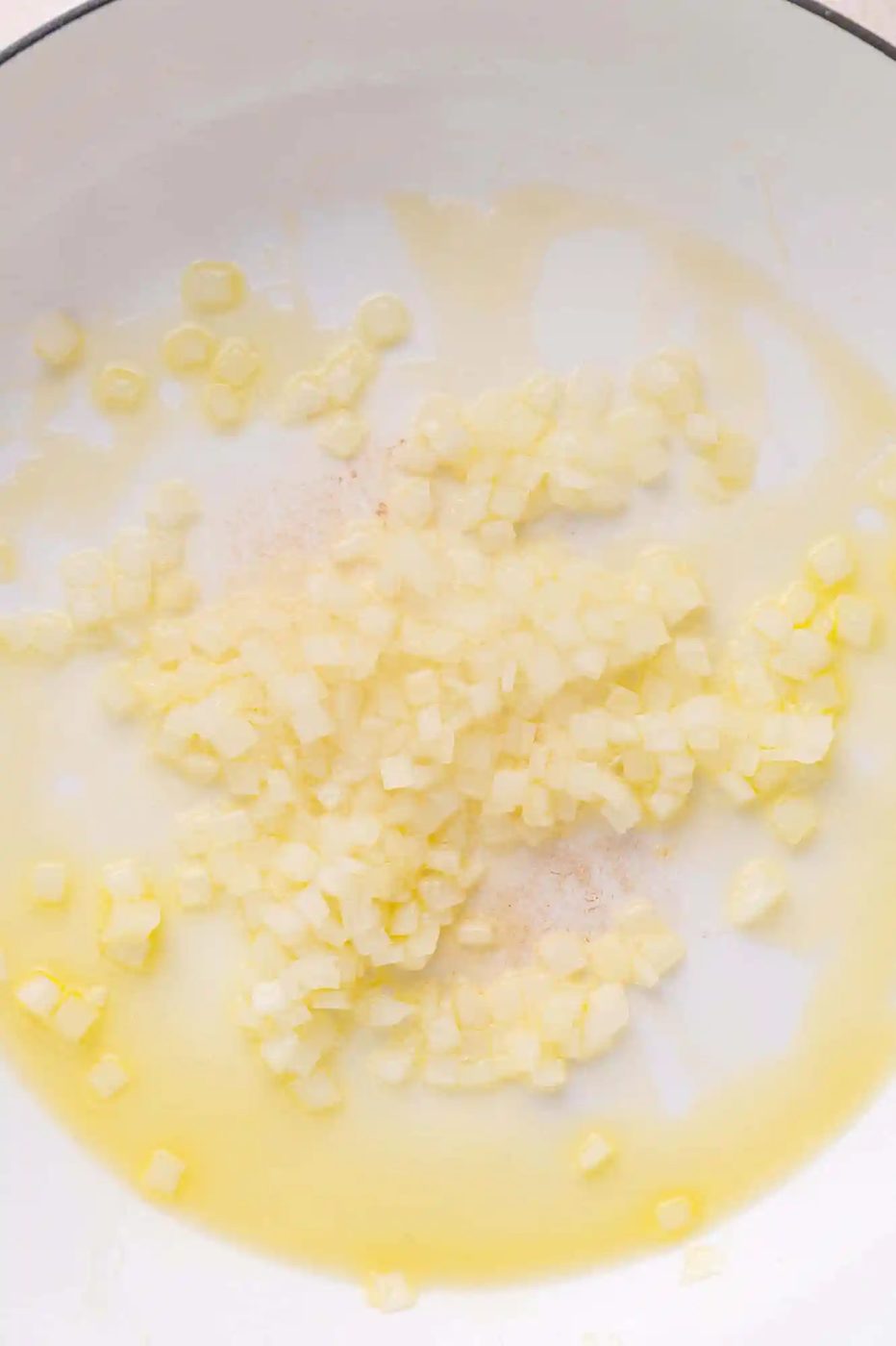Diced onions cooking in oil in a white pan.