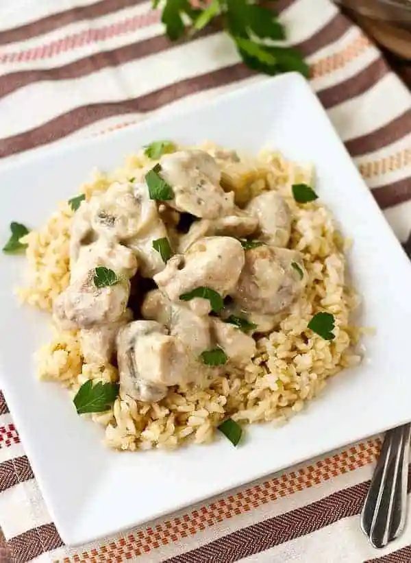 Overhead of chicken on rice on square white plate.
