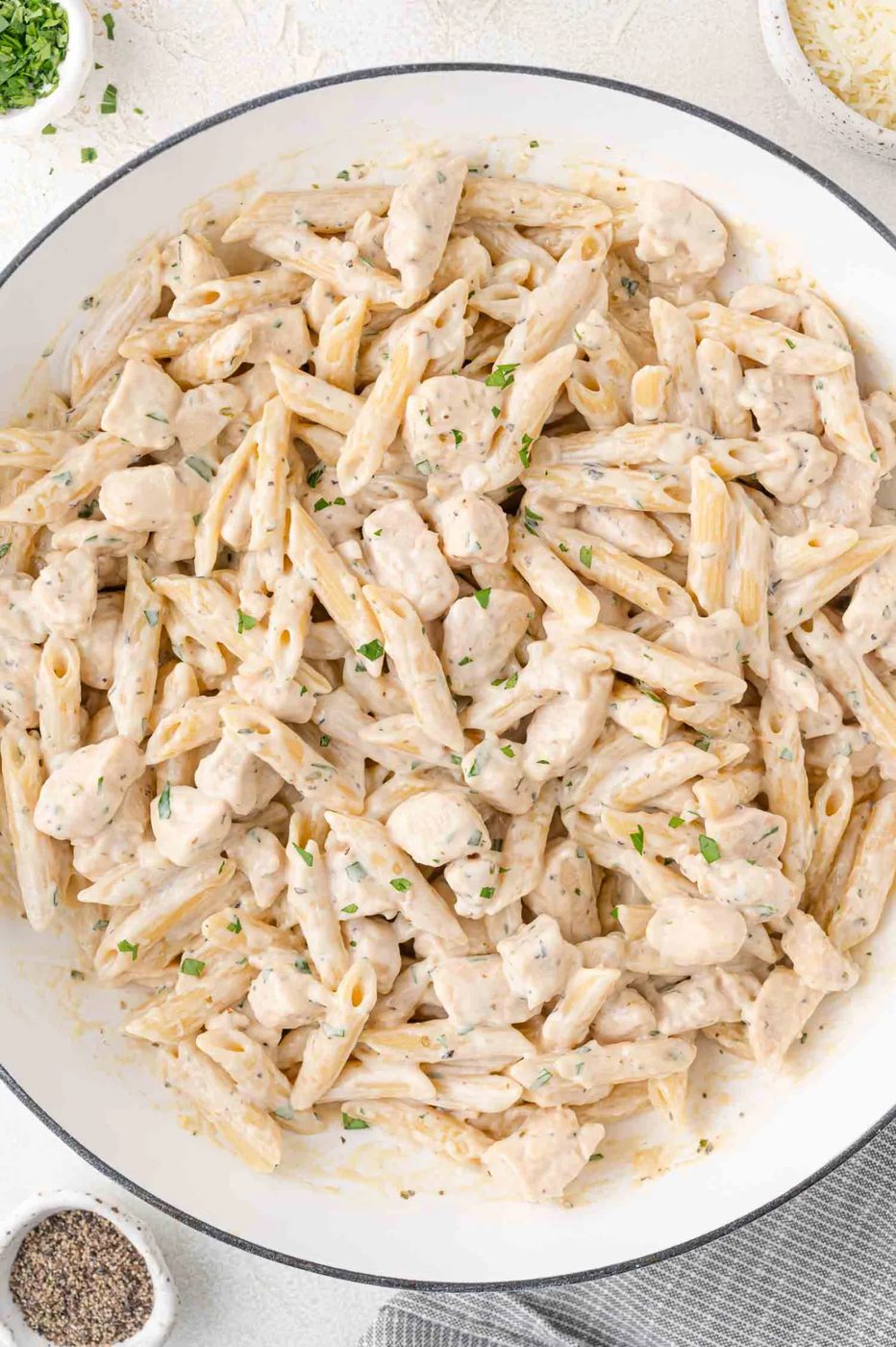 A close-up of a creamy pasta dish with penne and chunks of chicken, garnished with herbs, served in a white bowl.