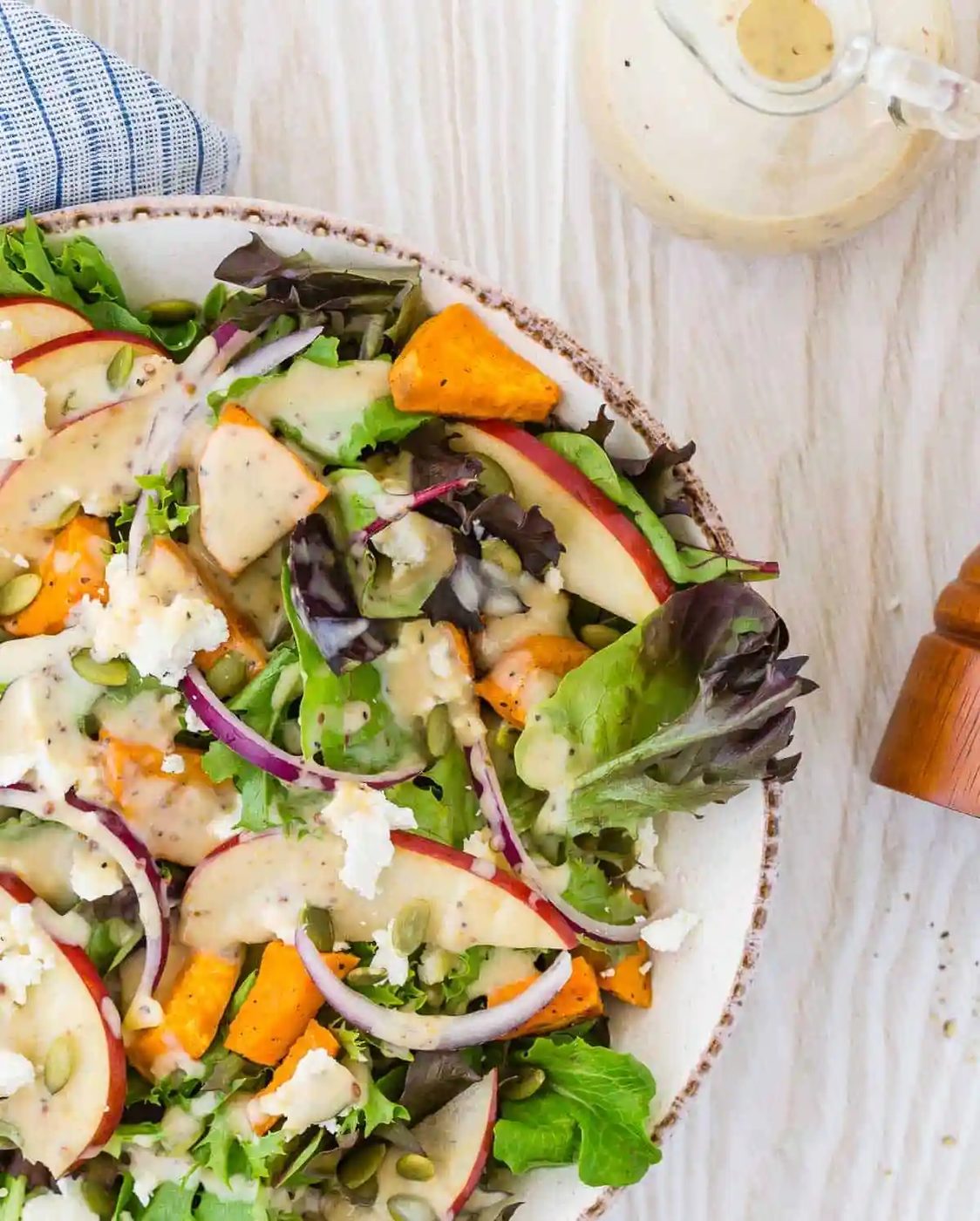 Colorful fall harvest salad with a creamy dressing on a light wood background.