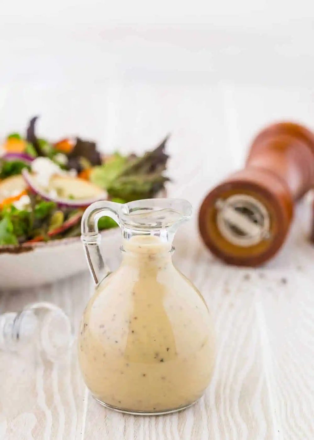 Creamy maple black pepper dressing in a small glass jar with a pour spout and handle.