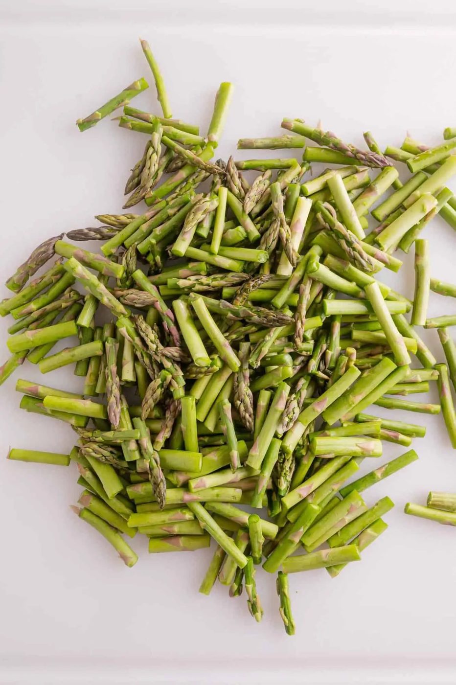 Chopped asparagus spears scattered on a white surface.