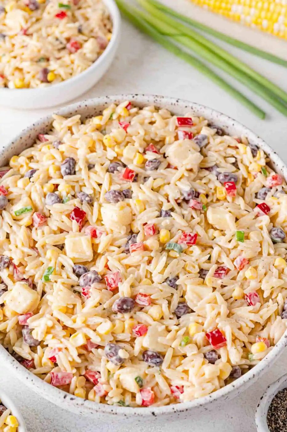 Orzo salad with black beans, corn, red bell peppers, and cheddar cheese, in a large bowl.