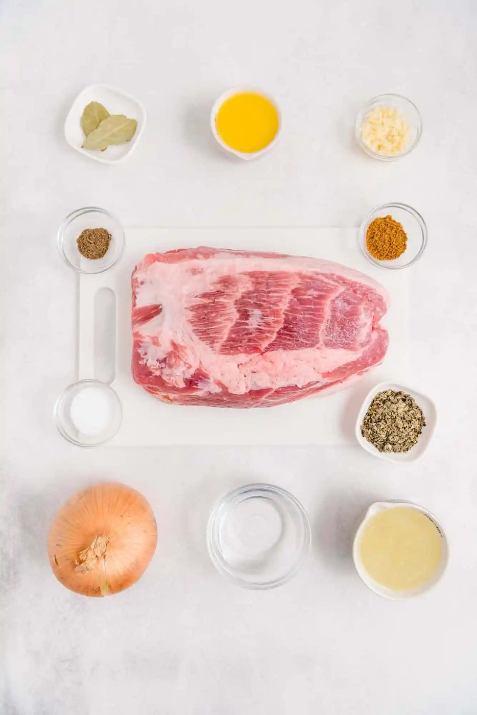 Overhead view of ingredients including pork shoulder, onion, spices, orange juice, and lime juice.
