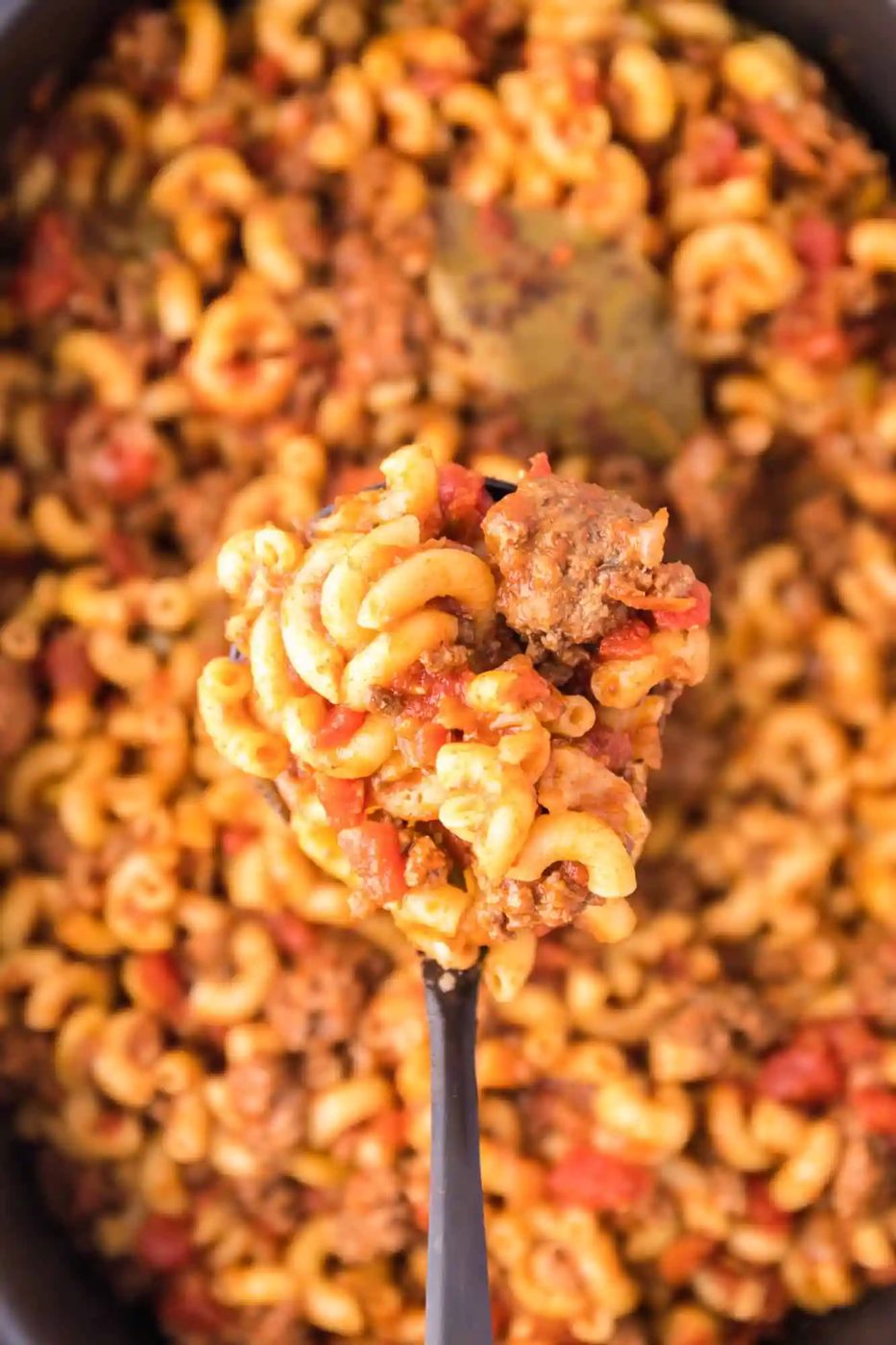 Overhead view of a large spoonful of goulash held over the slow cooker.