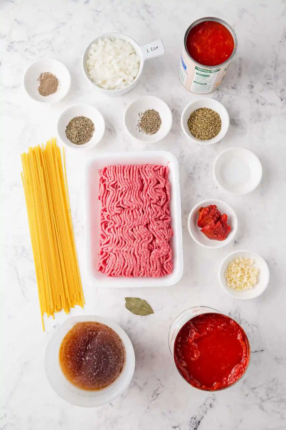 Ingredients for spaghetti on a marble surface, including ground meat, tomatoes, and more.