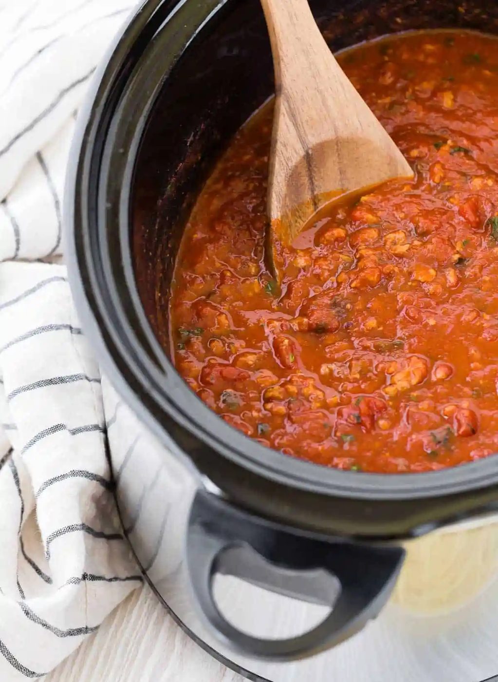 Wooden spoon in a crockpot of spaghetti sauce.