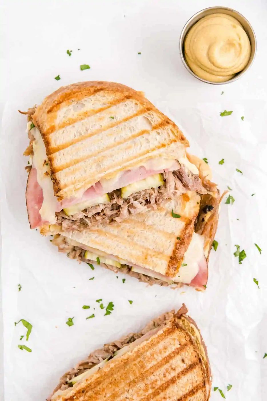 Overhead view of a cuban sandwich, cut in half, with a dish of mustard nearby.