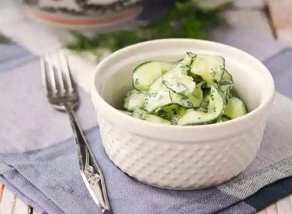 Front closeup of salad in white serving bowl, with fork and blue plaid napkin.