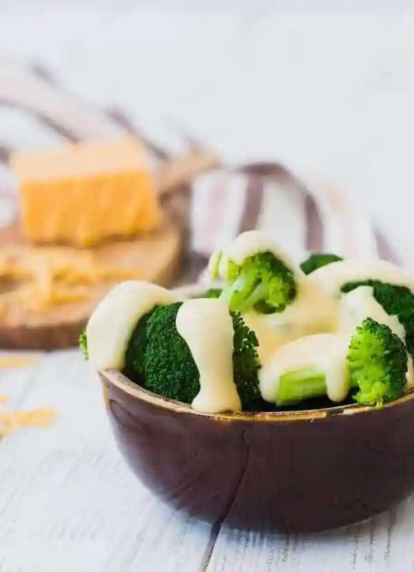Closeup of round brown bowl containing broccoli and cheese sauce.
