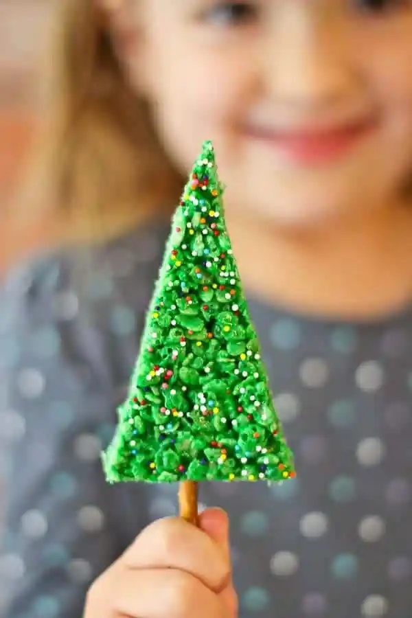 Front view closeup of Christmas tree cookie, held in hand, smiling girl in background.