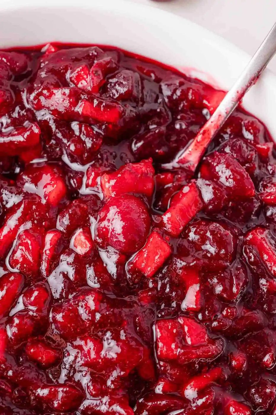 Close up of apple cranberry sauce on a spoon, in a white bowl.