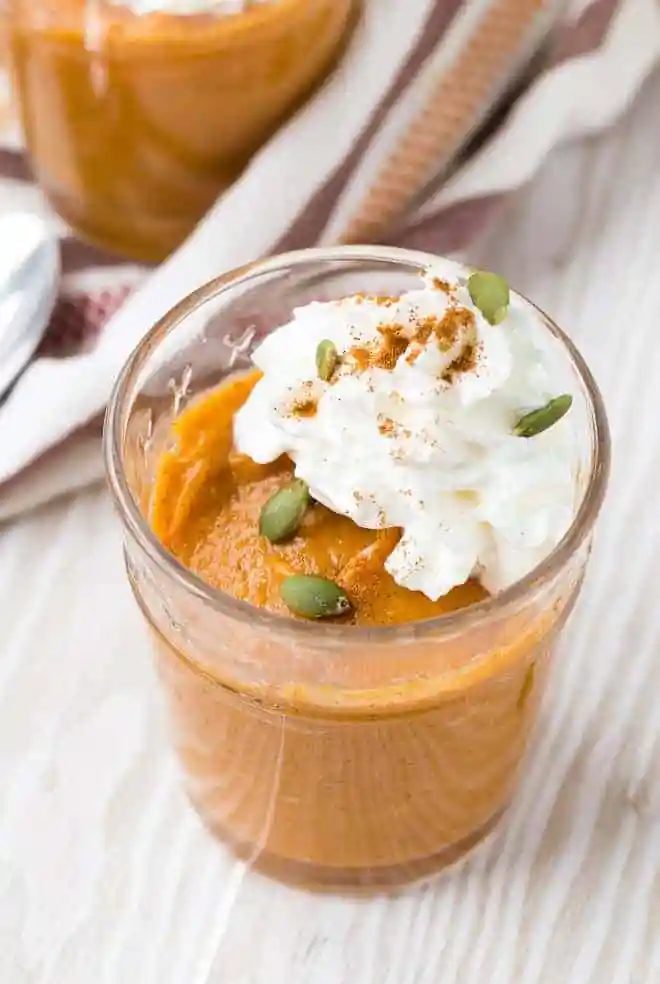 Close up view of straightforward pumpkin pudding garnished with whipped cream, pepitas, and cinnamon.