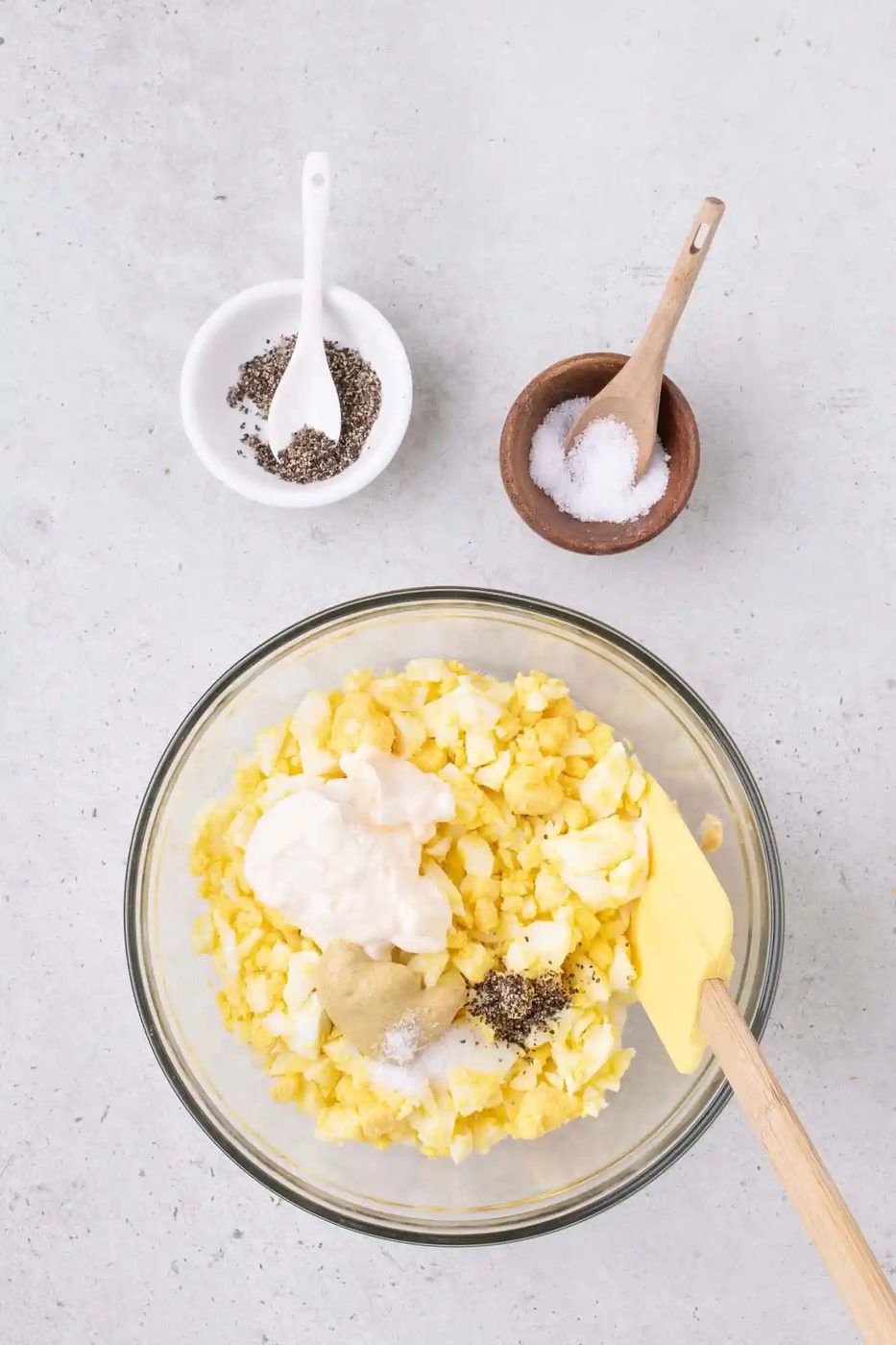 Bowl of egg salad with mayonnaise and mustard; small bowls of salt and pepper on the side.