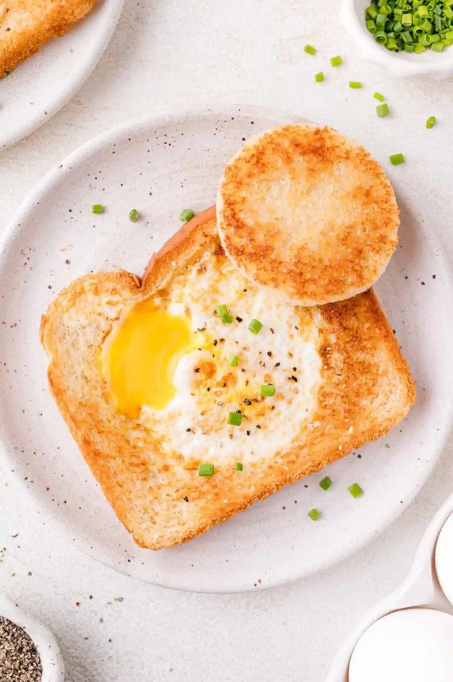 Egg in a basket garnished with chopped chives and served on a white plate.