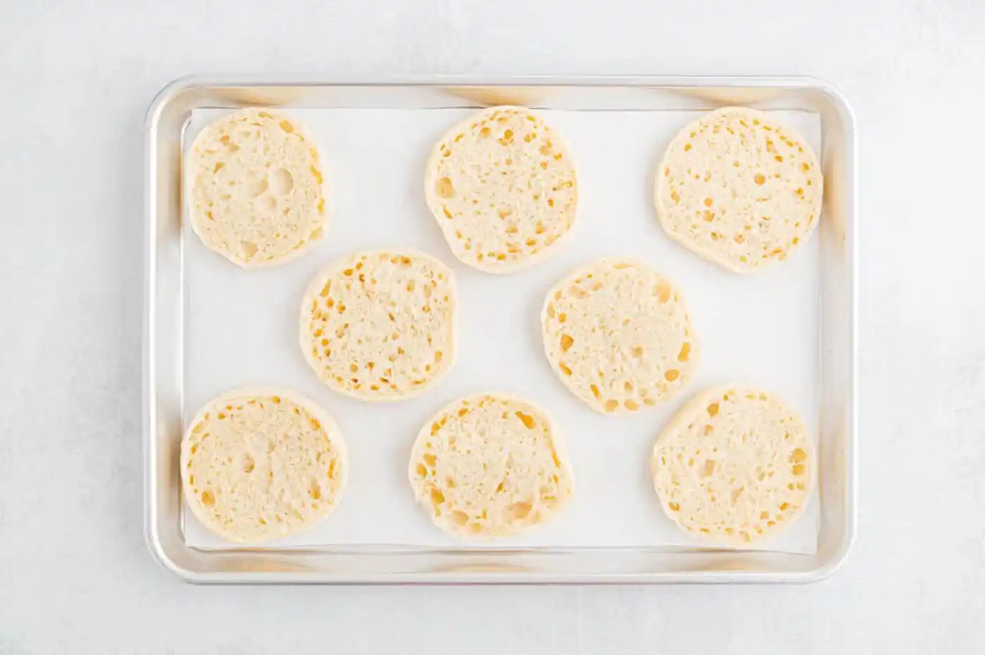 English muffins cut in half, on a sheet pan.