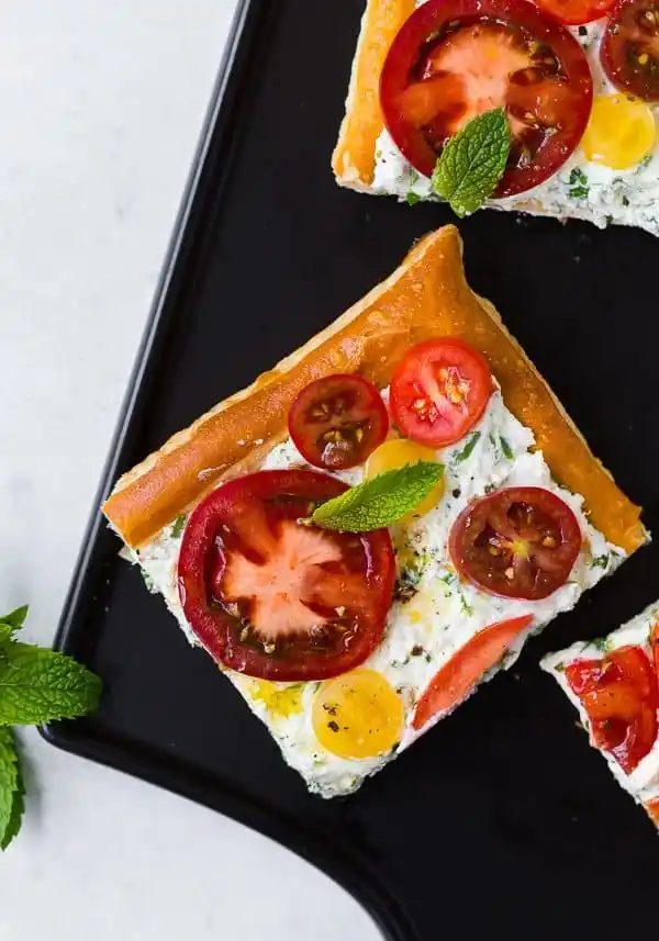 Overhead of sliced tart on a black pan, garnished with fresh mint.