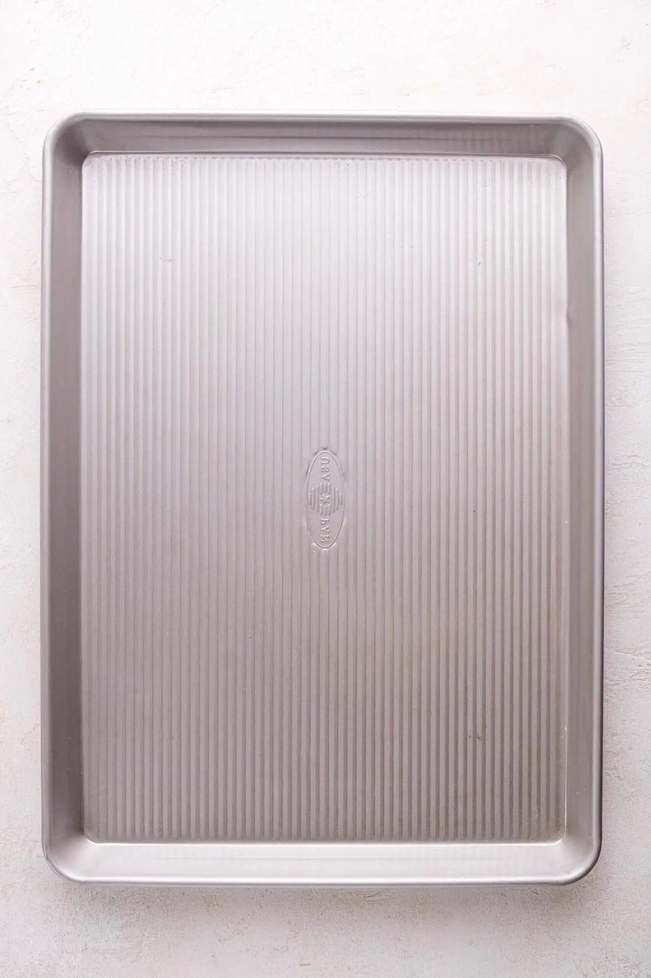A rectangular metal sheet pan with raised edges and a textured, ridged surface, placed on a light-colored background.