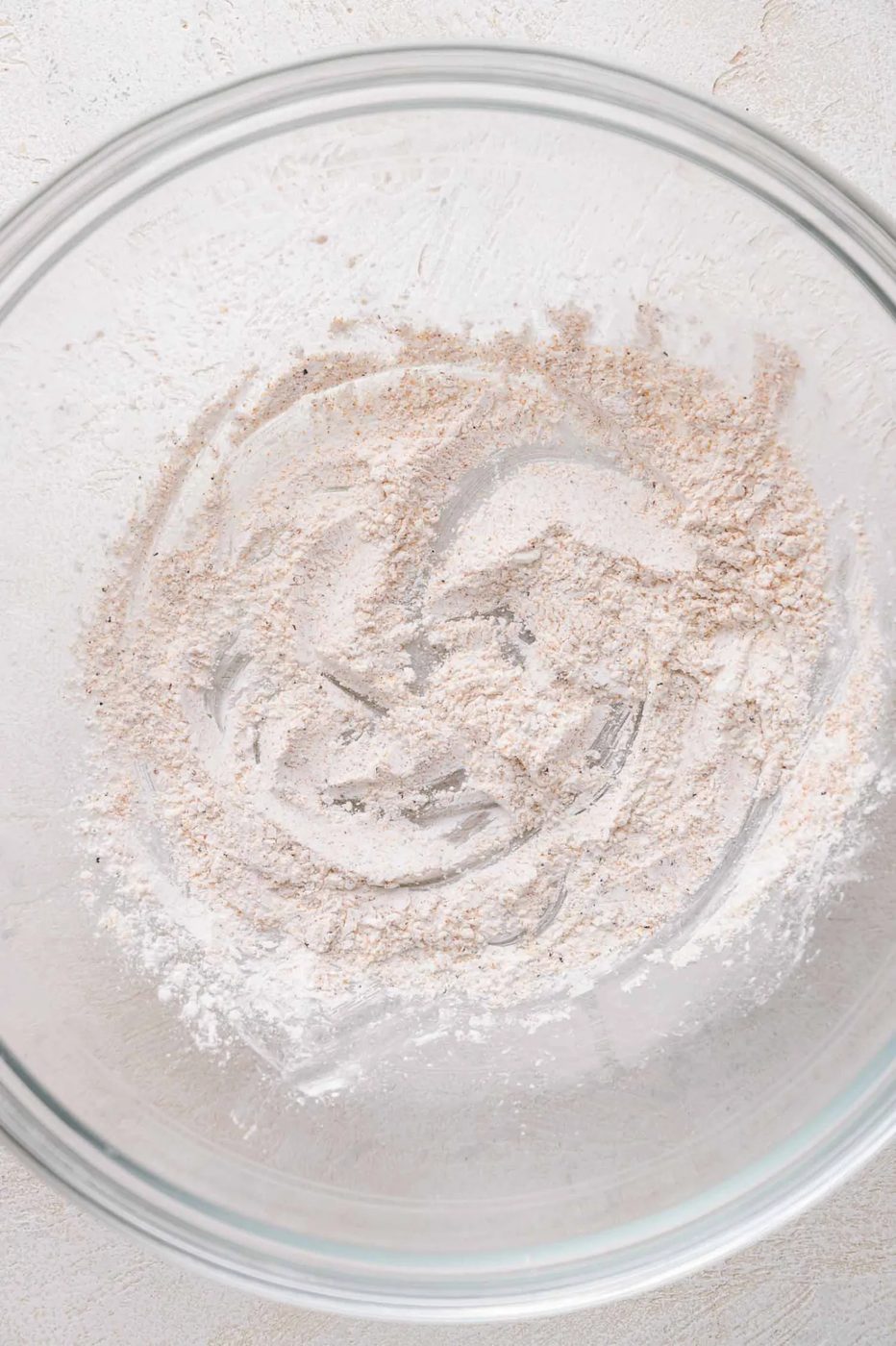 A clear glass mixing bowl contains a small amount of cornstarch on the bottom, lightly spread across the surface.