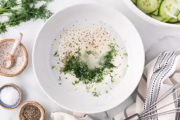 Dill and herbs added to a white bowl with sour cream.