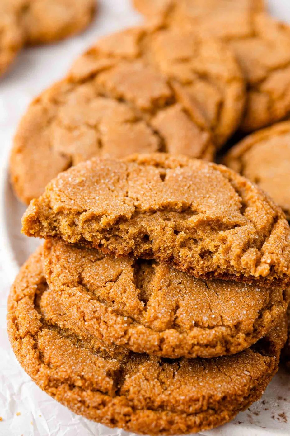 Close-up of a stack of ginger cookies, with one cookie broken in half, showing a soft interior and a sugar-coated surface.