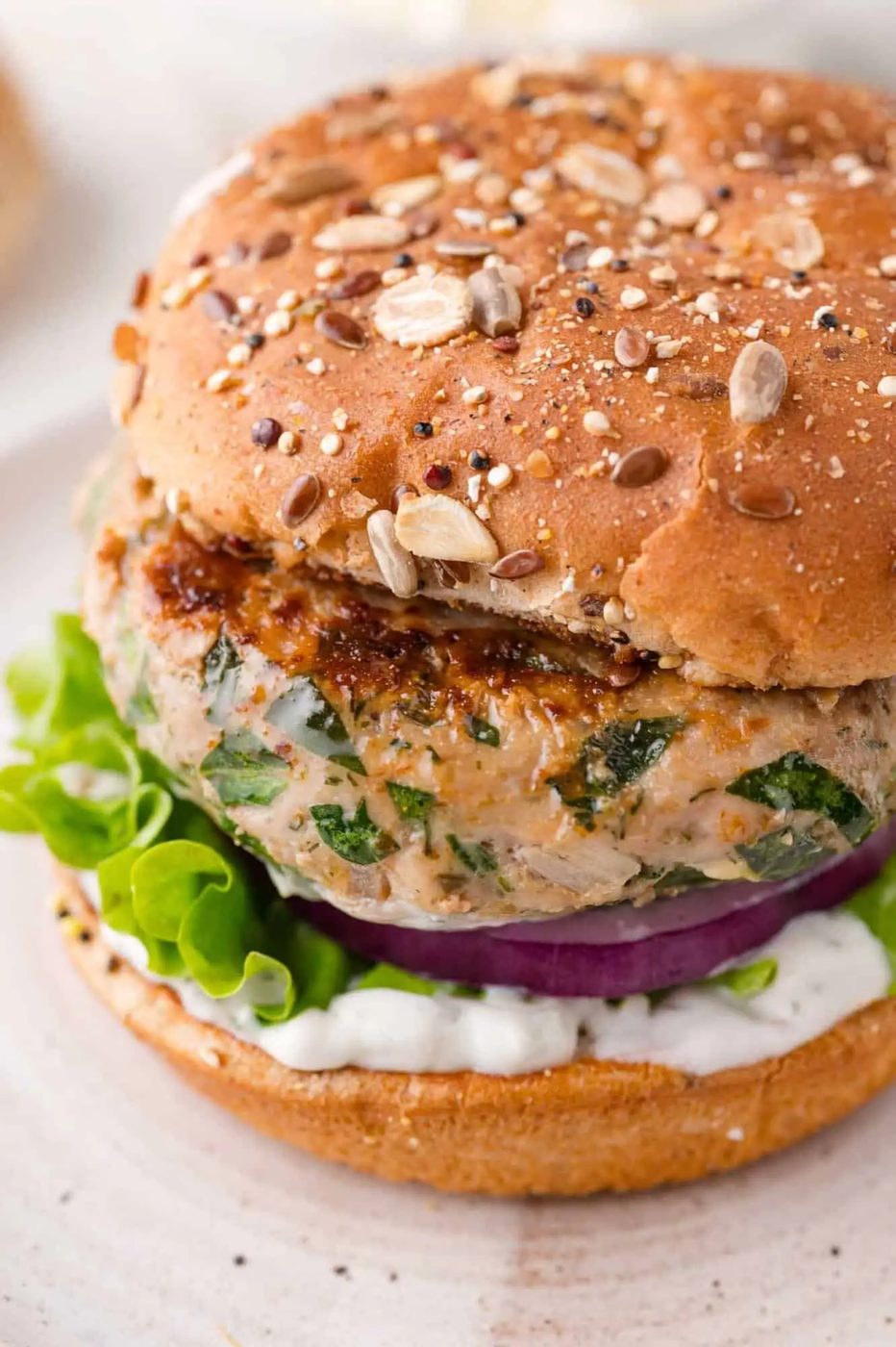 A close-up of a turkey burger on a whole grain bun with lettuce, red onion, and a white sauce.