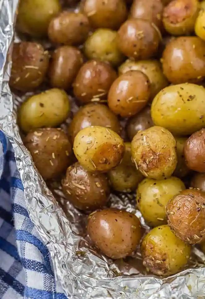 A pound and a half of baby potatoes, partially wrapped in foil. Specks of rosemary are pictured, as well as a blue and white linen.