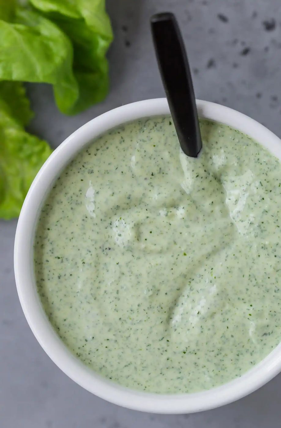 Close up of green goddess dressing in a white bowl.