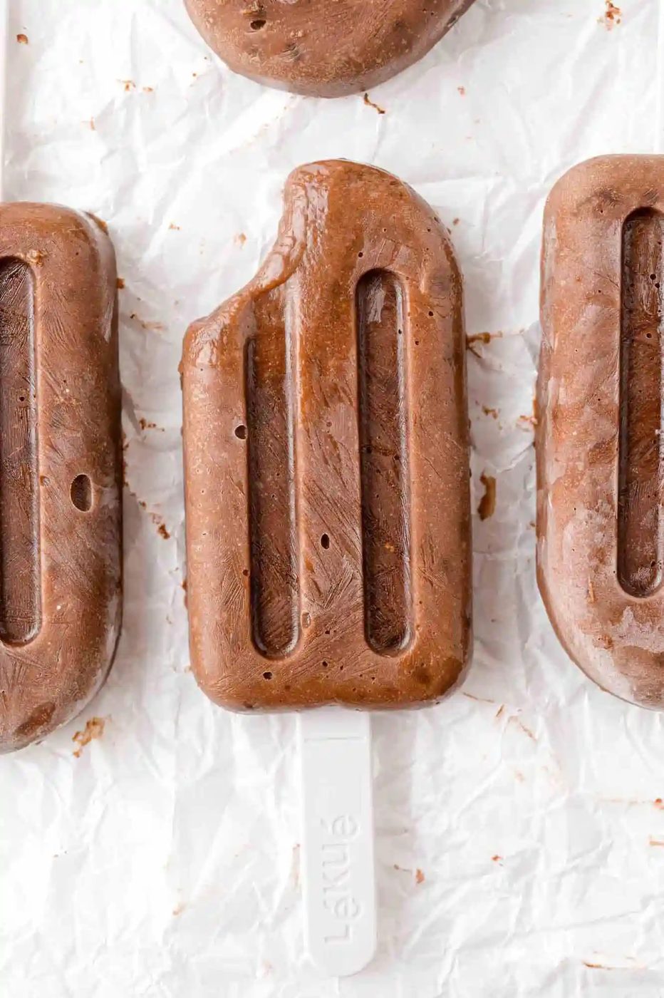 Three chocolate pudding pops, one with a bite removed.